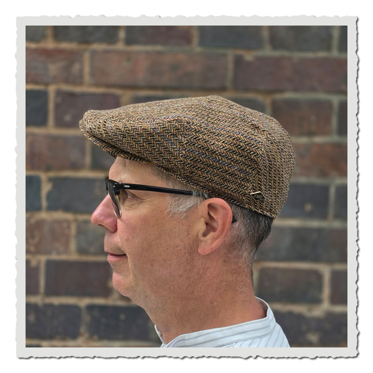 Seitenansicht einer klassischen Schiebermütze von JJ Hats in Driver-Cap-Form aus reiner Schurwolle. Die Mütze besitzt ein braun-beiges Fischgrätenmuster mit feinen blauen Linien und einen kleinen, fest vernähten Schirm.