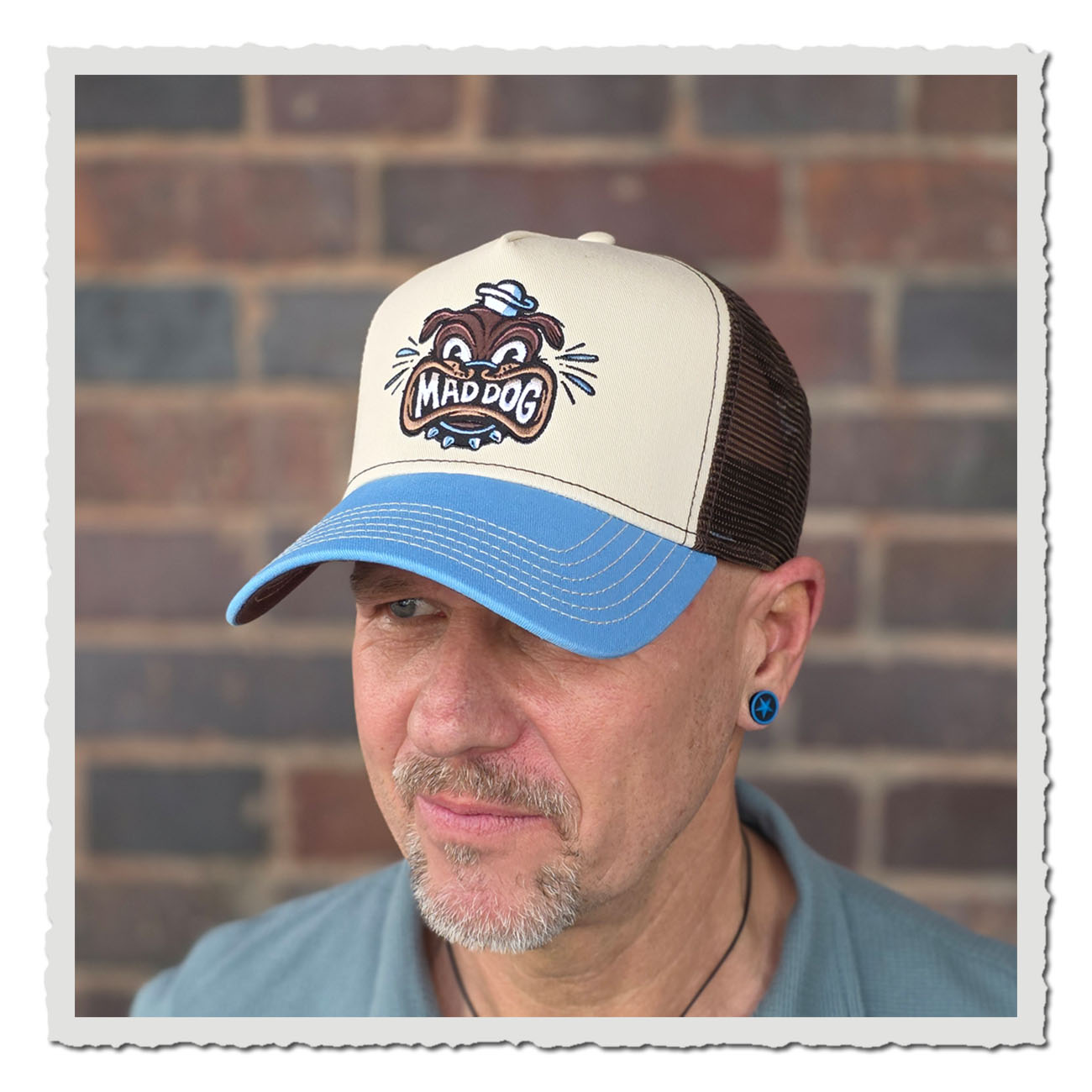 Mann vor Steinmauer trägt Beige-blauesJJ Hats Cap im Vintage Look mit markantem Bulldoggen-Stickmotiv und Mesh