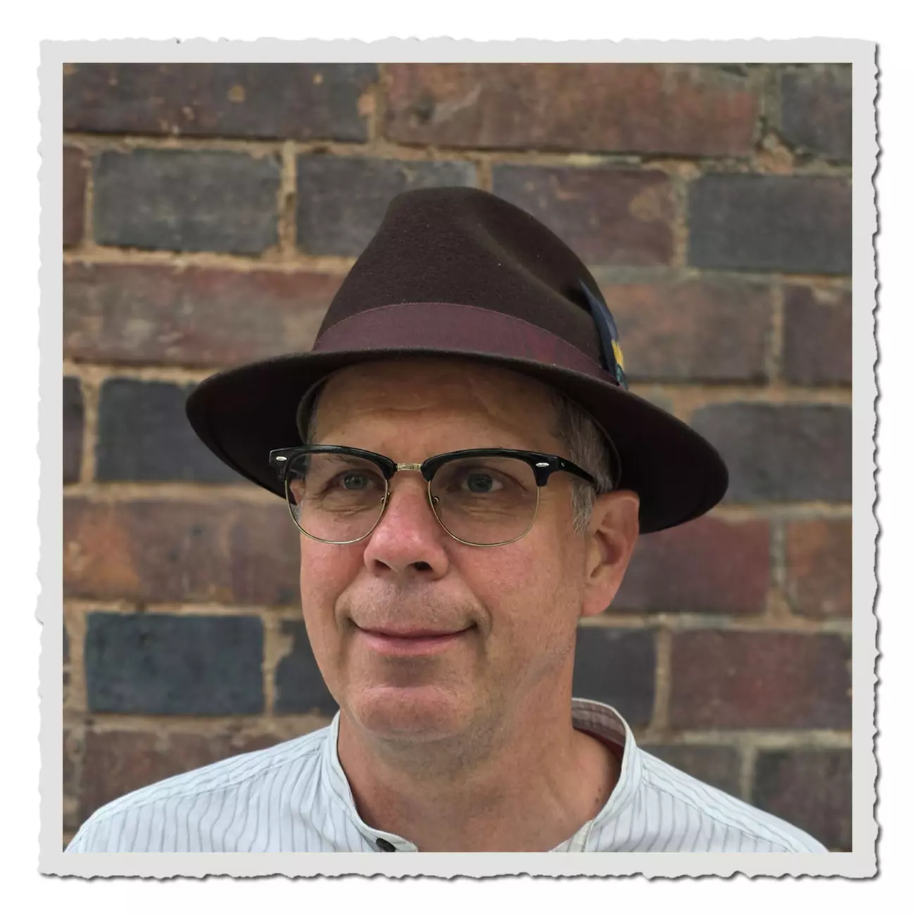 Vorderansicht des Fedora-Hutes Lite Felt von JJ Hats aus schokobraunem Wollfilz. Der Hut hat eine mittlere Krempe, ein weinrotes Ripsband und seitlich eine dezente Federverzierung.