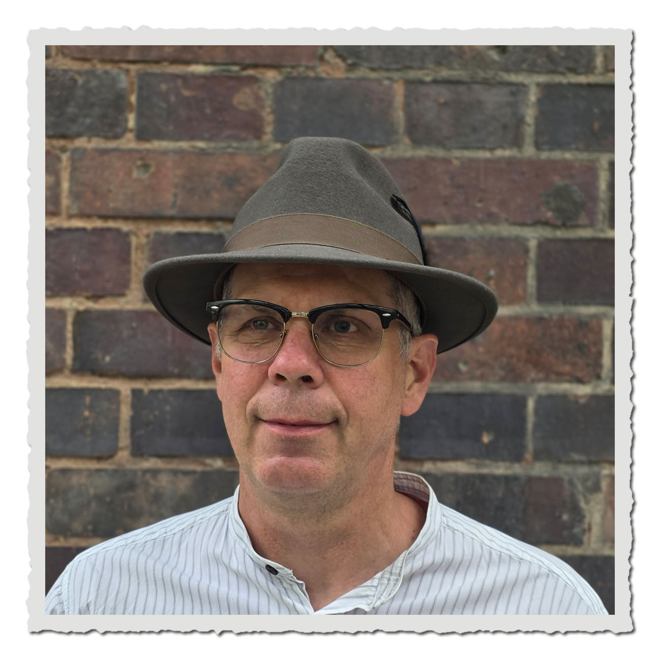 Vorderansicht eines Fedora-Hutes der Marke JJ Hats aus grauem Wollfilz. Der Hut hat eine klassische Form mit mittlerer Krempe, ein braunes Ripsband und eine seitliche Feder als Zierde.
