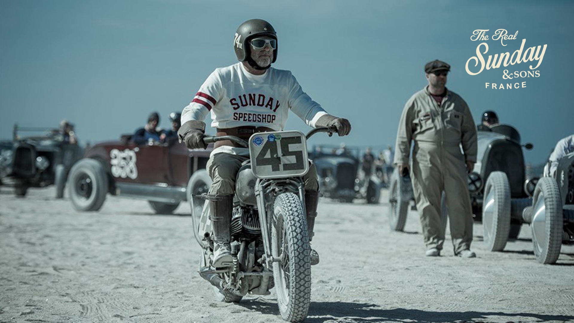 Vintage-Rennszene: Fahrer mit Helm und "Sunday Speedshop"-Pullover nimmt an einem Strandrennen teil.